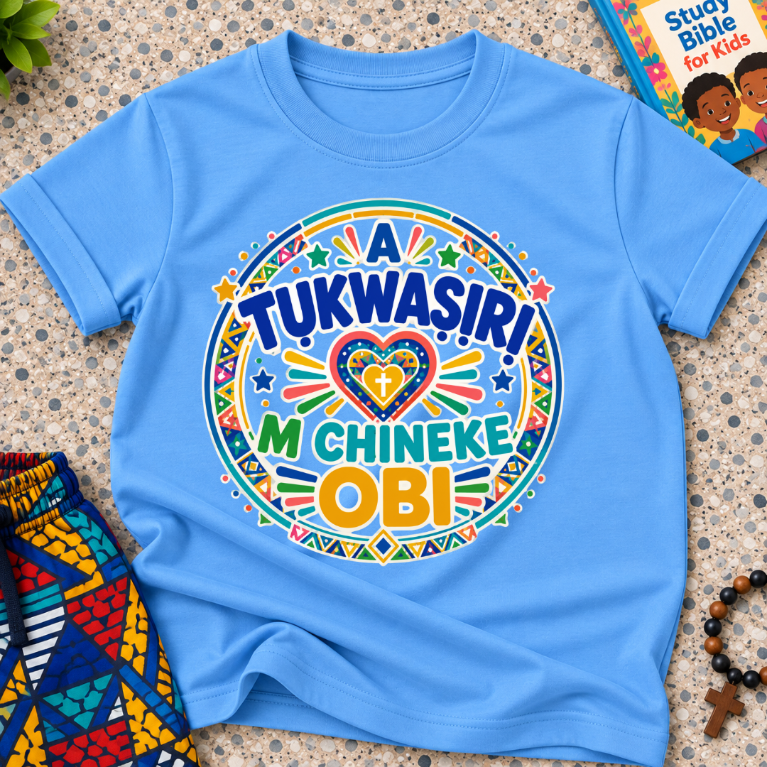 A Tukwasiri M Chineke Obi Igbo-language kids shirt in light blue featuring colourful lettering, a heart motif, and circular decorative patterns
