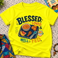 Blessed Loved and Well Fed Christian kids shirt in yellow featuring colourful food and family-inspired artwork
