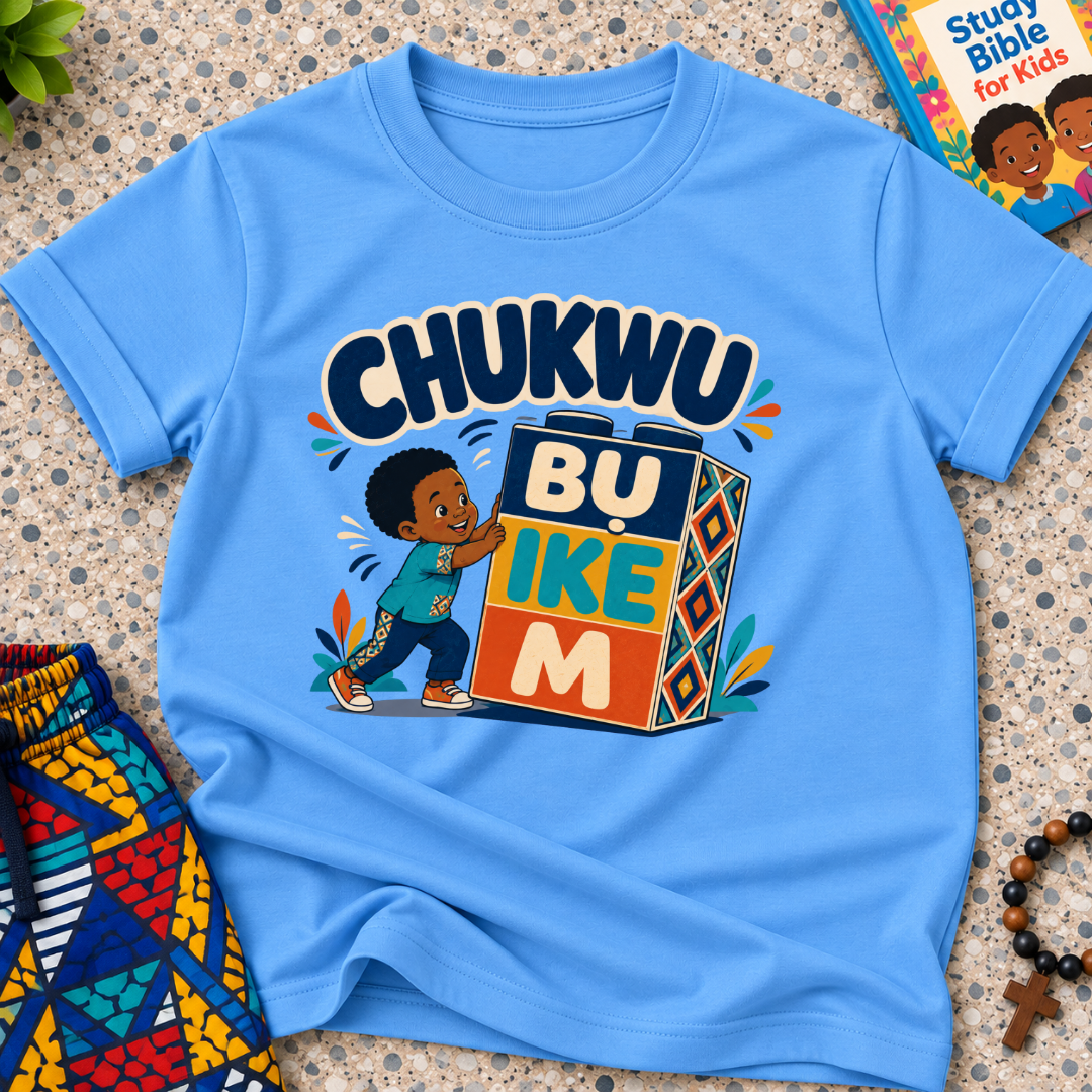Chukwu Bụ Ike M Igbo Christian kids shirt in light blue featuring bold lettering and a child beside colourful blocks
