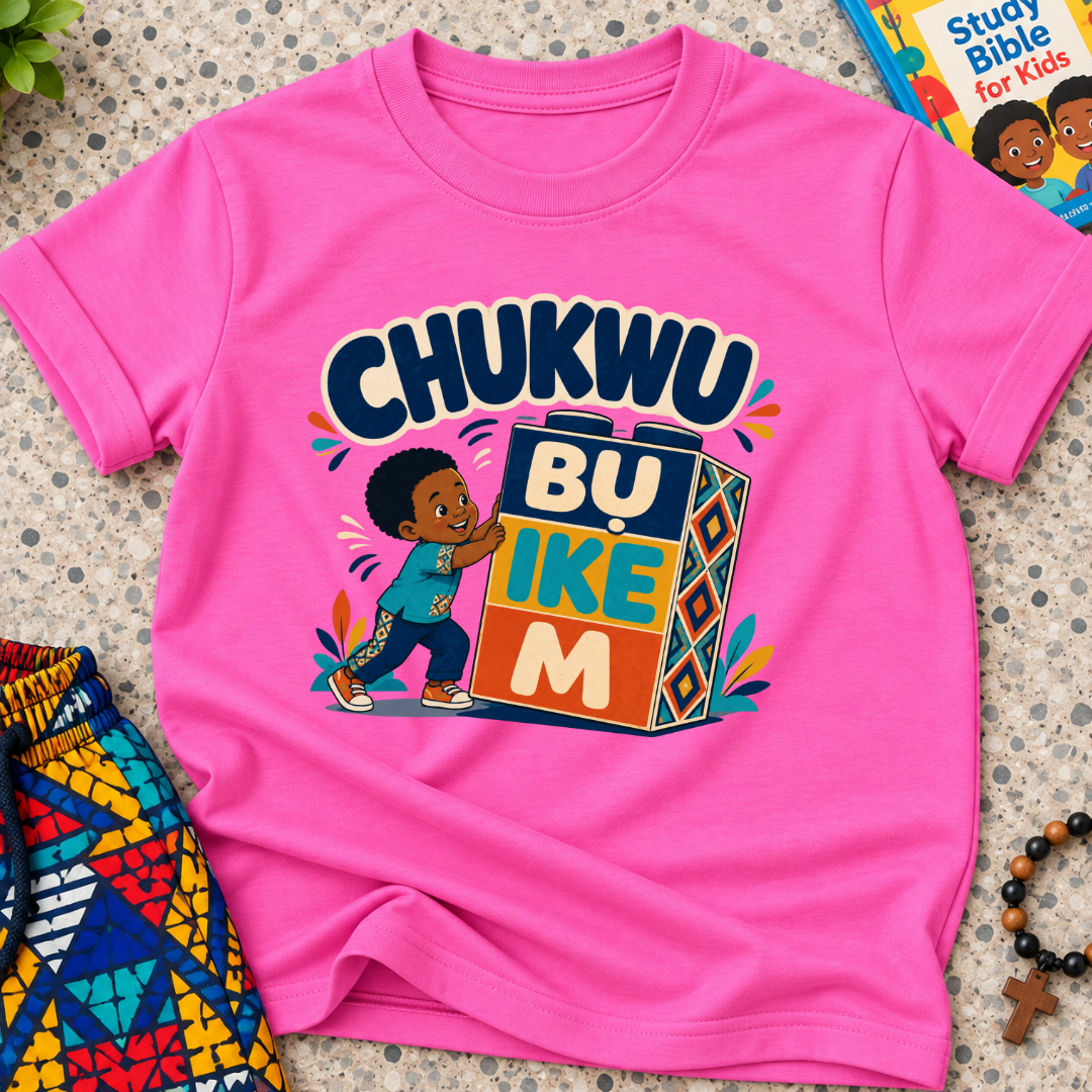 Chukwu Bụ Ike M Igbo Christian kids shirt in pink featuring bold lettering and a child beside colourful blocks
