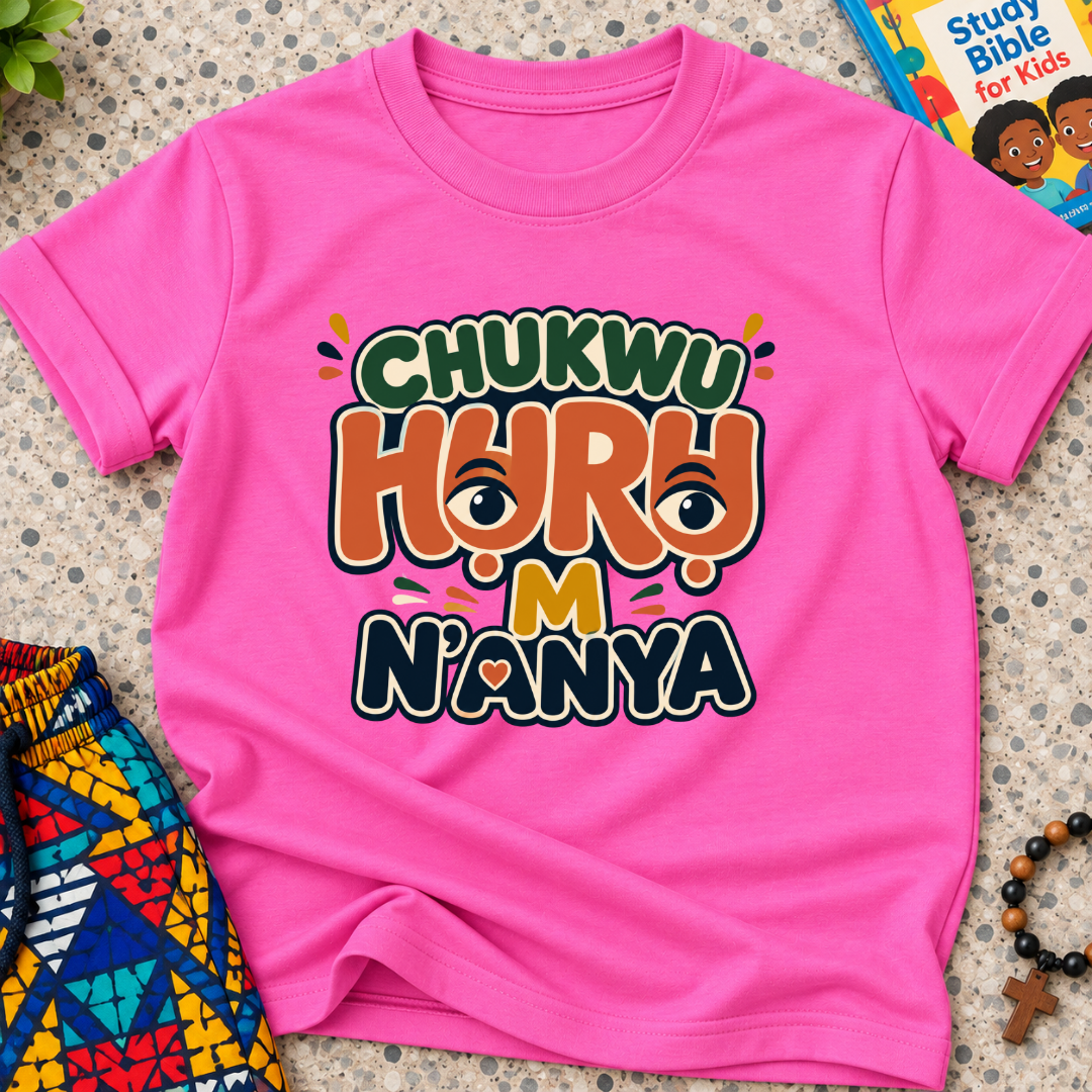 Chukwu Huru M N'anya Igbo Christian kids shirt in pink featuring bold colourful lettering and decorative artwork
