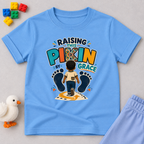 Raising This Pikin by Grace Christian kids shirt in light blue featuring a child illustration and playful Nigerian parenting message
